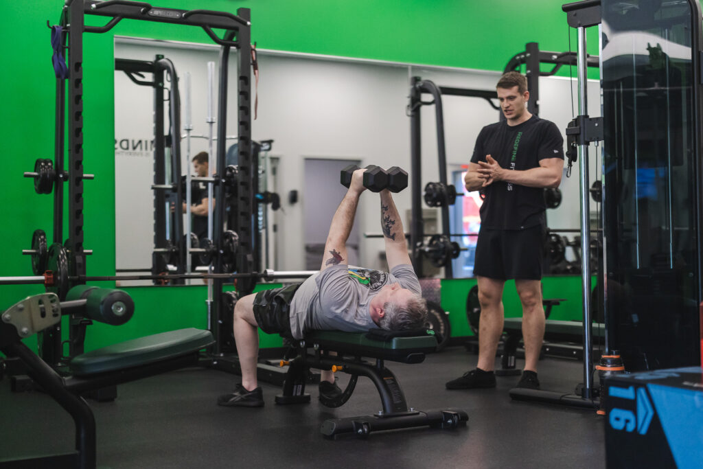 A Fitness Specialist spotting a client on the floor at Redefine Fitness Stony Brook