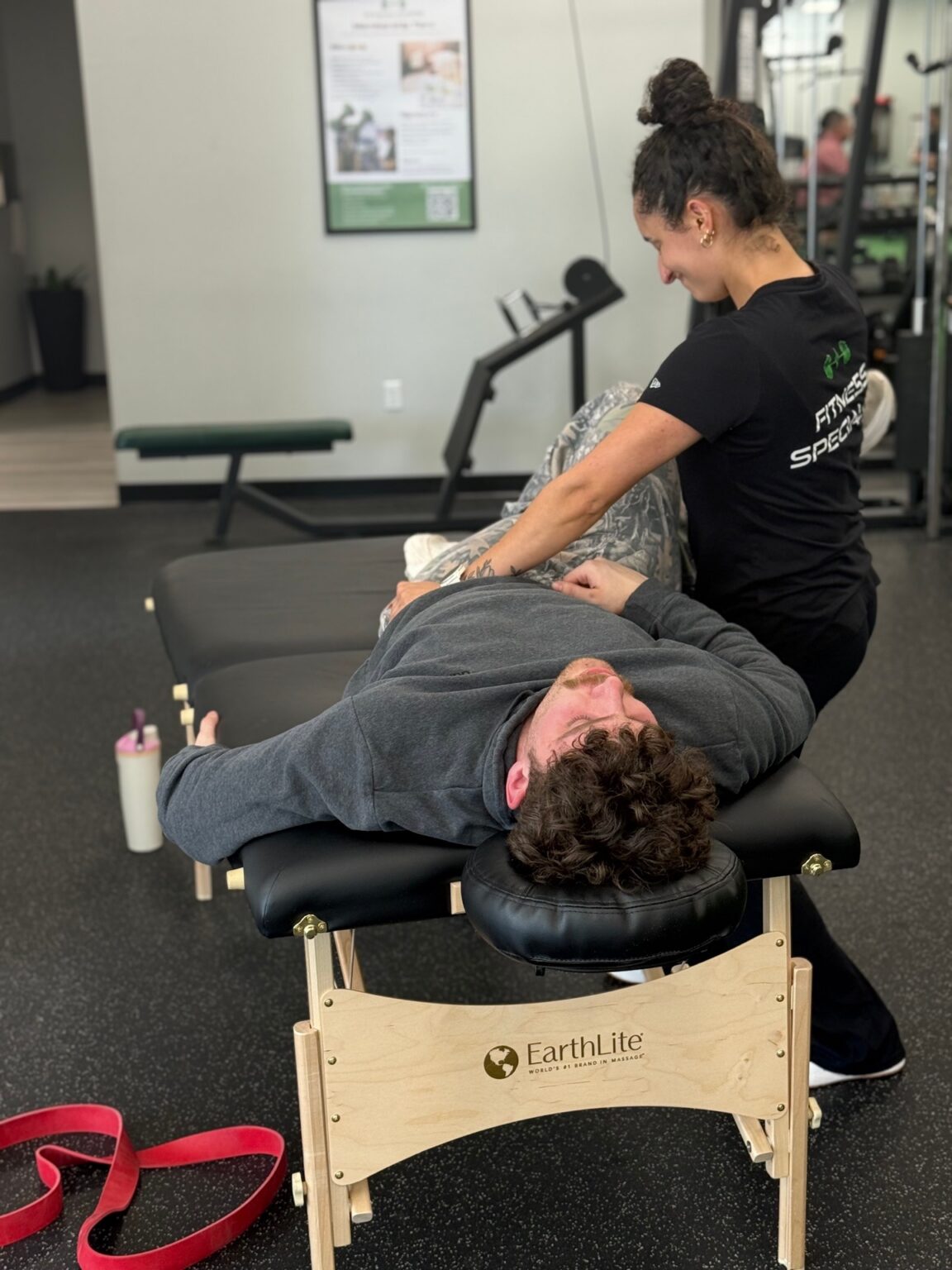 Fitness Specialist guiding a client through an assisted hamstring stretch on the table